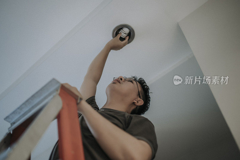 an asian chinese mid adult male changing light bulb in living room, apartment home